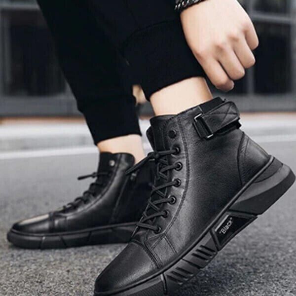 A person wearing black high-top sneakers with laces and a side buckle.