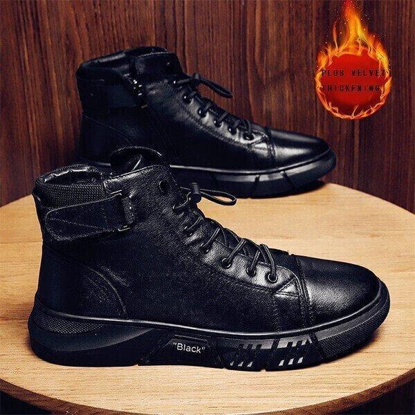 A pair of black high-top sneakers with laces, displayed on a wooden surface.