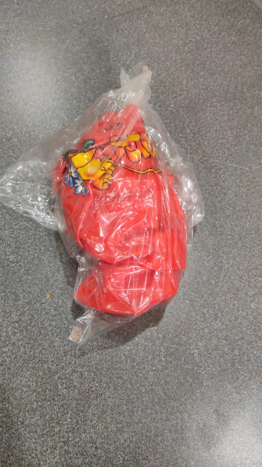 A transparent plastic bag containing a red object with a cartoon fruit illustration, placed on a gray surface.