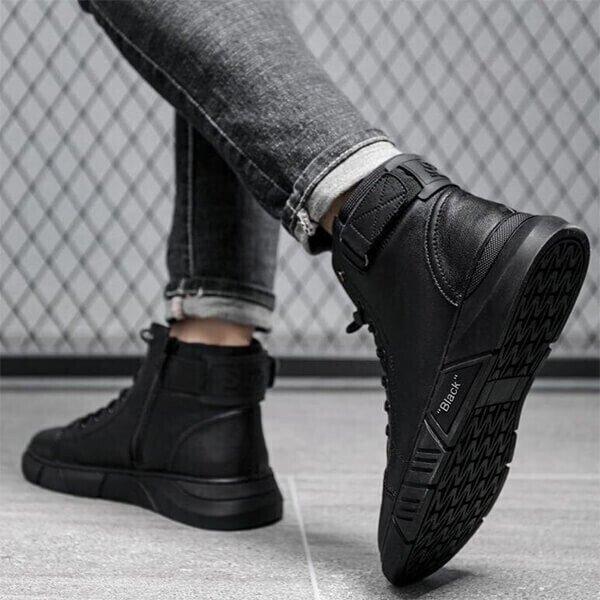 A person wearing black high-top sneakers and rolled-up jeans standing on a tiled floor.