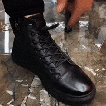 A person tying the laces of a shiny black leather boot on a marble floor.
