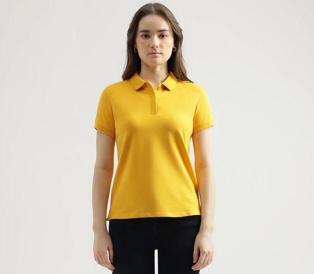 A person wearing a yellow short-sleeve polo shirt and black pants standing against a plain light background.