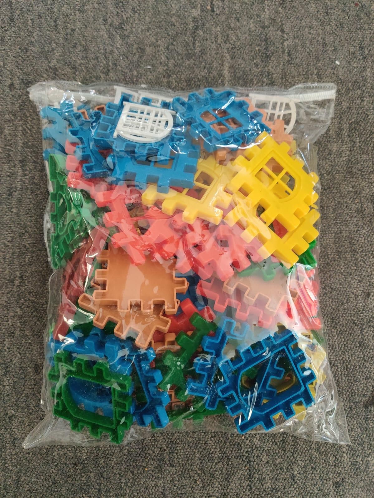 A clear plastic bag filled with colorful plastic interlocking building pieces on a gray textured surface.