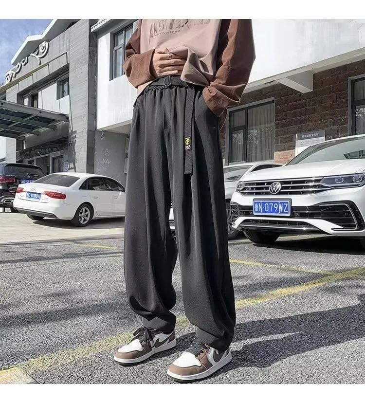 A person wearing loose black pants and brown sneakers standing in a parking lot with cars in the background.