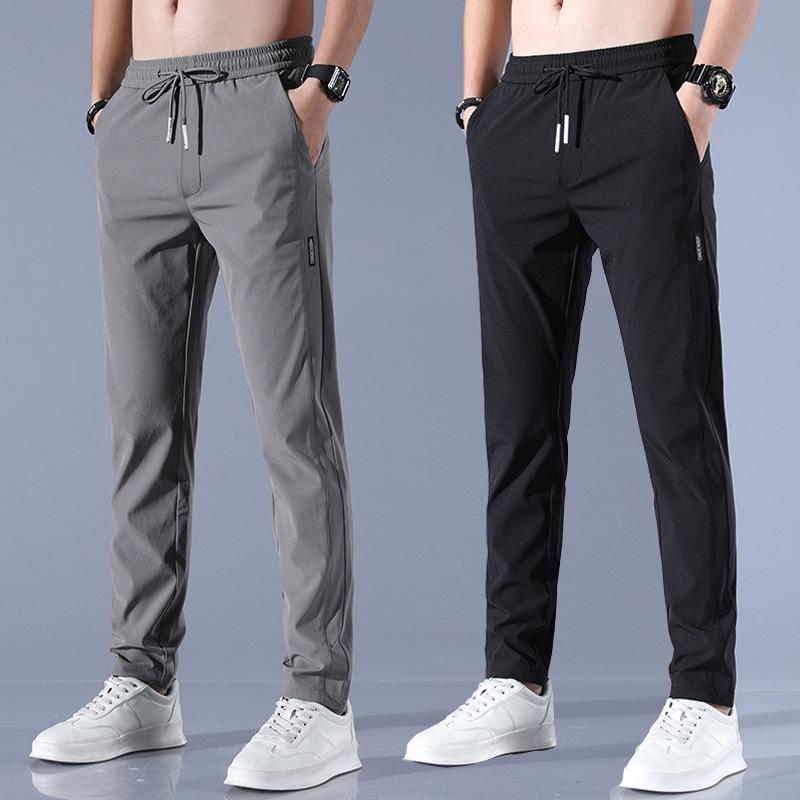 Two male models wearing drawstring jogger pants, one in grey and one in black, both paired with white sneakers.