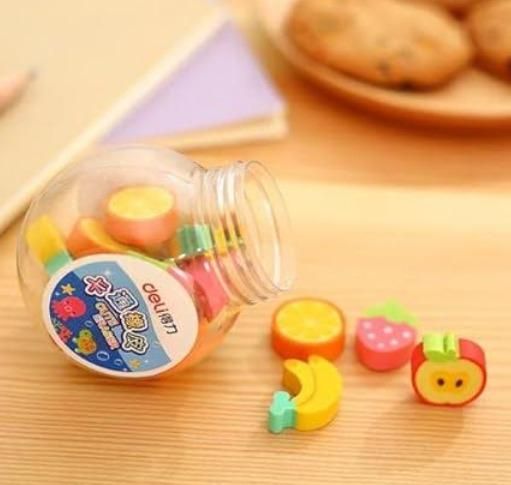 A plastic jar filled with colorful fruit-shaped erasers, with some erasers taken out and placed on a wooden surface.
