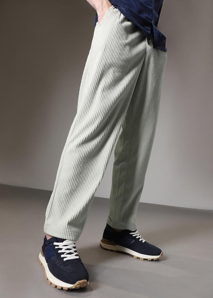A person wearing light green textured pants and navy sneakers.