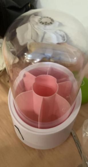 A white and pink plastic container with a transparent dome lid, placed on a wooden surface.