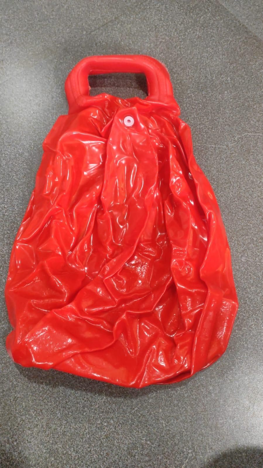 A red plastic collapsible water bag with a handle, placed on a dark countertop.