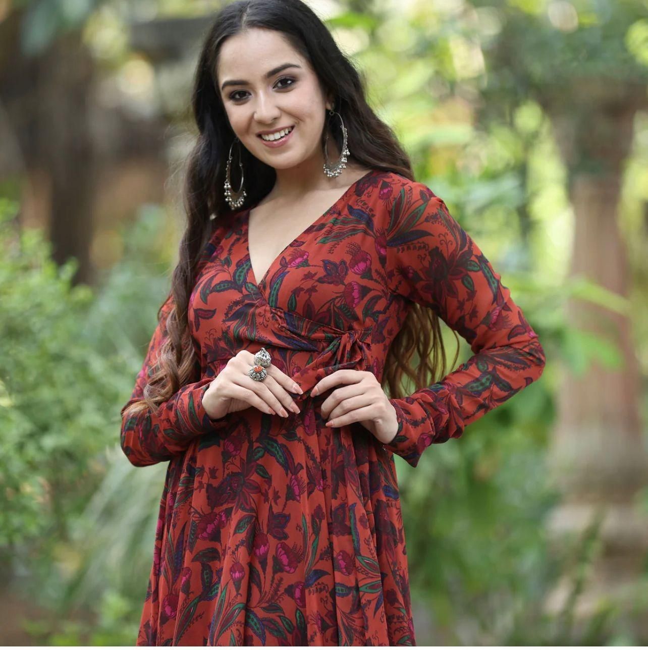 A woman in a long-sleeved, red floral dress posing outdoors and smiling.