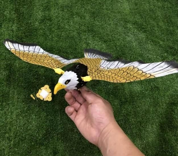 A hand holding a toy mechanical bird with wide wings, designed to look like an eagle, on a grassy surface.