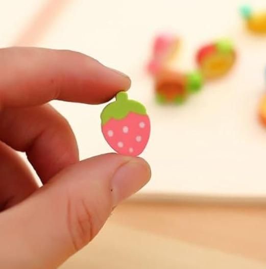 A hand holding a small pink strawberry-shaped eraser with white dots and a green top.