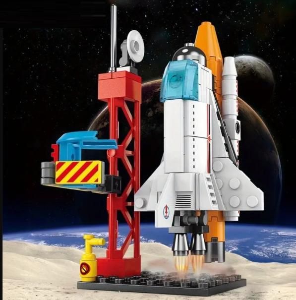 A toy space shuttle built from interlocking plastic bricks on a launch pad with a space background.