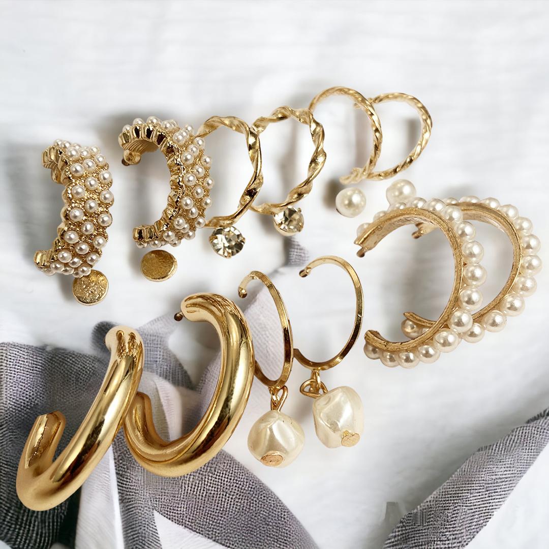 An assortment of gold and pearl earrings displayed on a white fabric background.