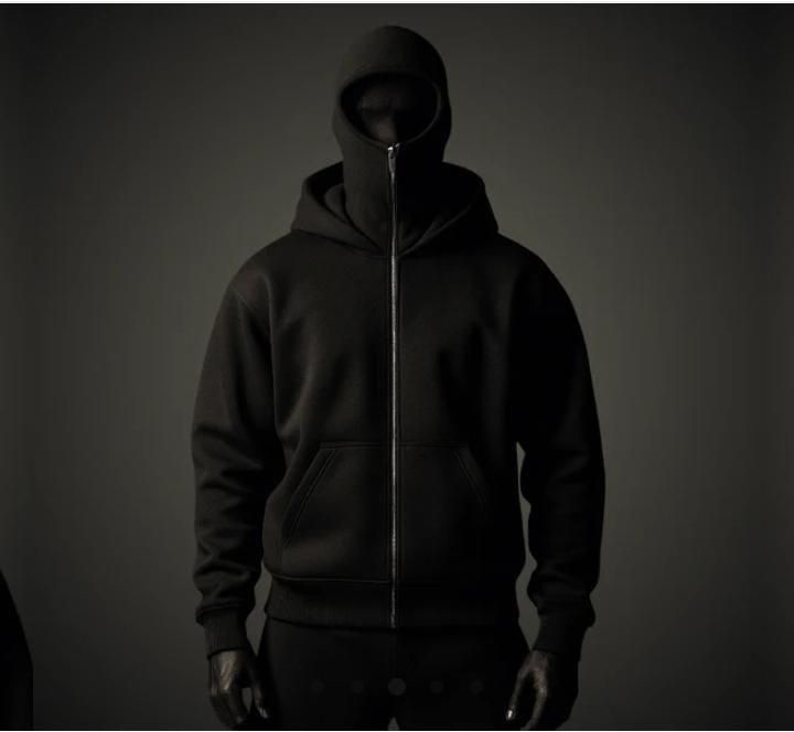 A person wearing a black zip-up hooded sweatshirt with a high collar that covers their lower face, set against a dark background.