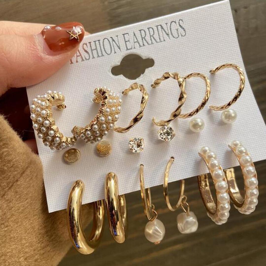 A hand holding a display card with assorted gold and pearl stud and hoop earrings.
