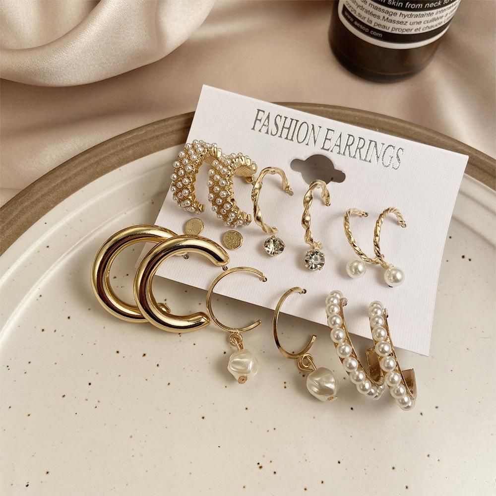 A set of six pairs of gold and pearl earrings displayed on a card labeled 'Fashion Earrings' on a ceramic plate.