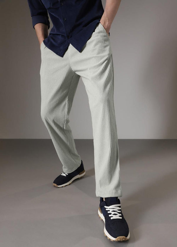 A person wearing light gray corduroy pants, a dark blue shirt, and navy sneakers with white laces.
