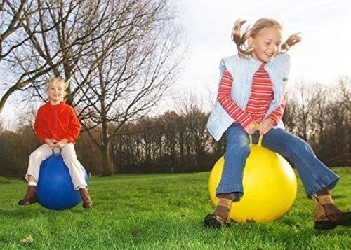 Two children bouncing on large inflatable balls outdoors on a grassy field.