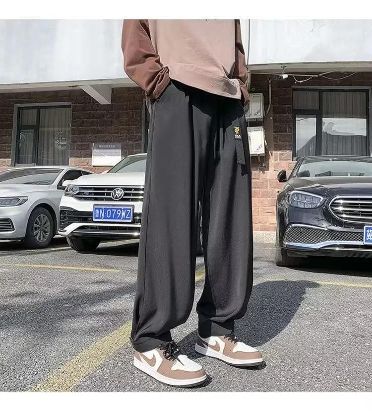 A person wearing loose black pants and brown sneakers standing in a parking lot with cars in the background.