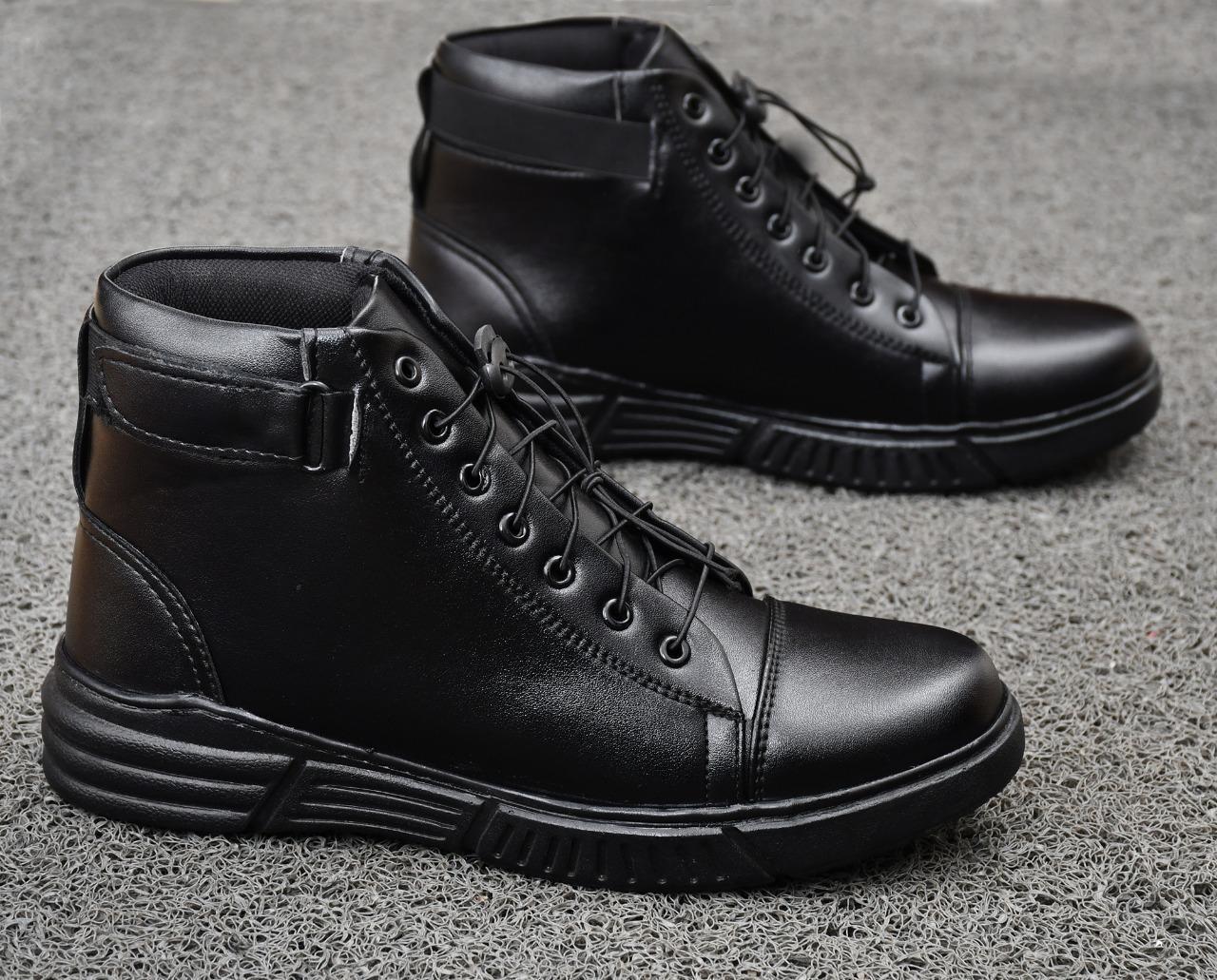 A pair of black high-top lace-up shoes on a textured gray surface.