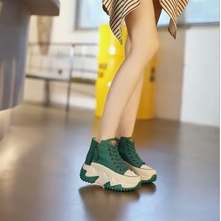 A person wearing a striped skirt and green high-top platform sneakers with chunky white soles.
