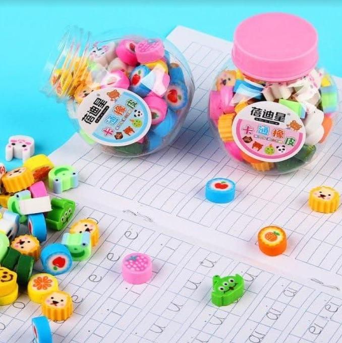 Two jars of colorful erasers shaped like various fruits and animals, scattered on handwriting practice sheets.