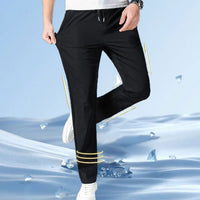 A person wearing black athletic pants with yellow stripes and white sneakers against a blue background.