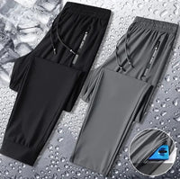 Two pairs of athletic pants, one black and one gray, displayed on a water droplet surface with a waterproof fabric illustration.