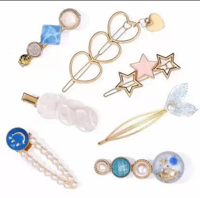 A collection of decorative hairpins and barrettes with various designs including pearls, stars, hearts, a mermaid tail, and colorful accents arranged on a white background.
