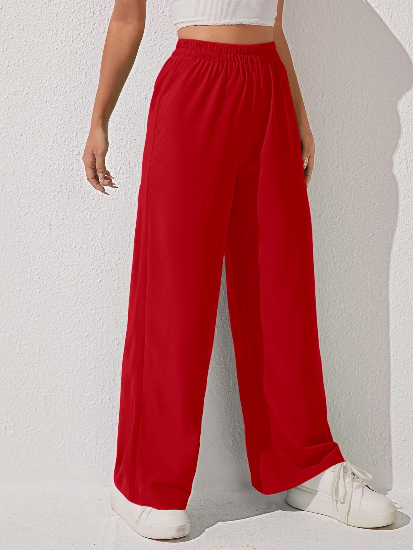 A person wearing bright red wide-leg pants and white sneakers, with a white top visible, standing against a light textured wall.
