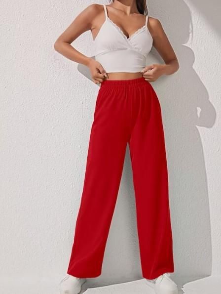 A person wearing loose bright red pants and a white crop top standing against a white wall.