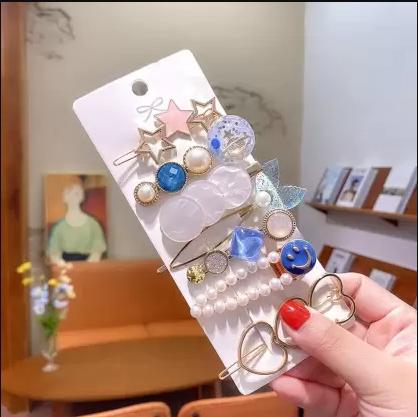 A hand holding a set of decorative hair clips with various designs including stars, pearls, and colorful shapes.