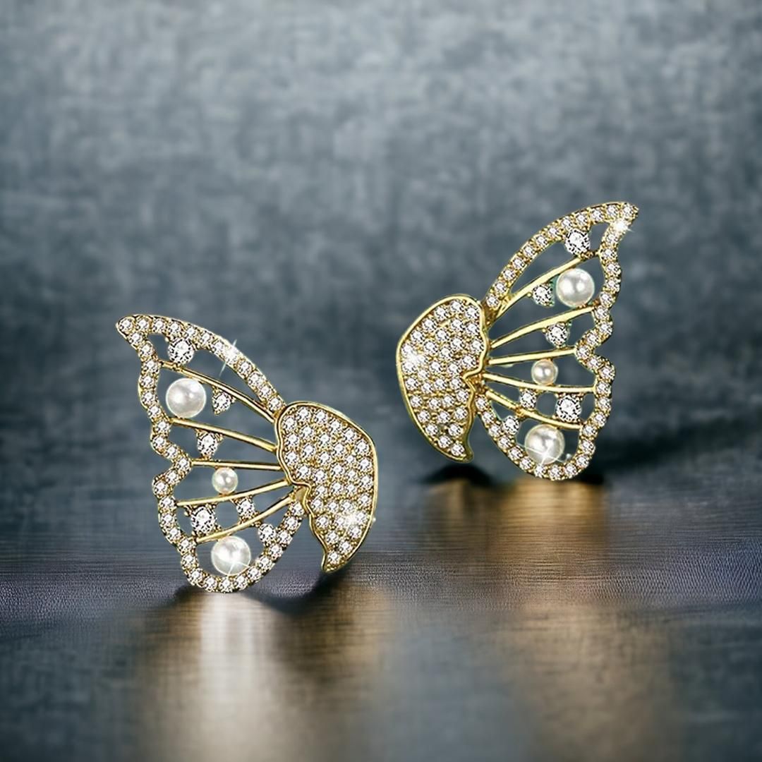 A pair of butterfly-shaped gold earrings encrusted with diamonds and accented with pearls.