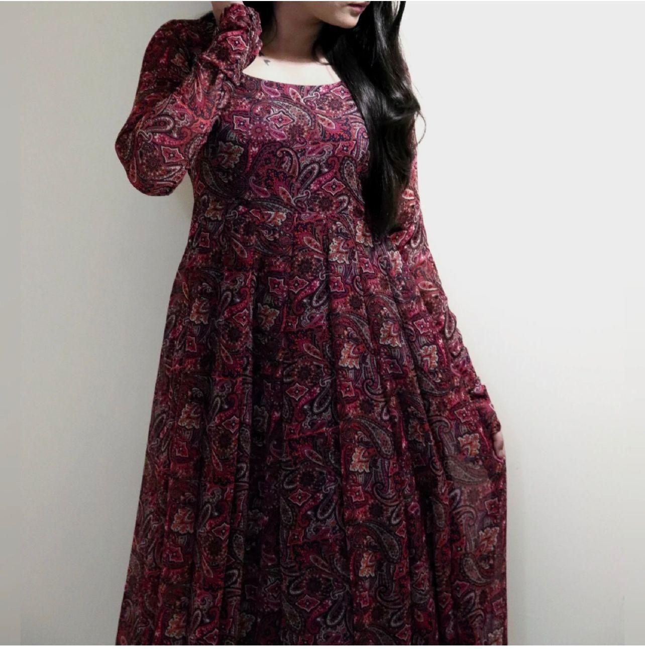 A woman wearing a long-sleeved, ankle-length dress with a red and purple paisley pattern.