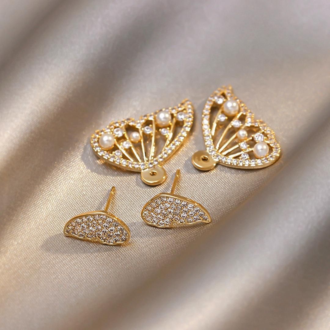A set of gold and crystal earrings with pearl accents, arranged on a shiny fabric surface.